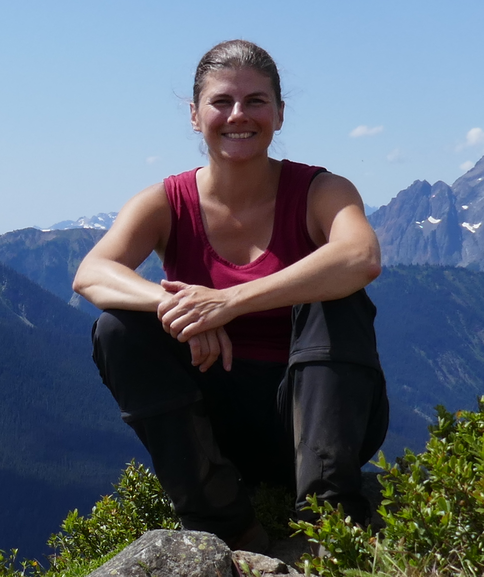 A woman sits smiling with a view of mountains in tthe background.