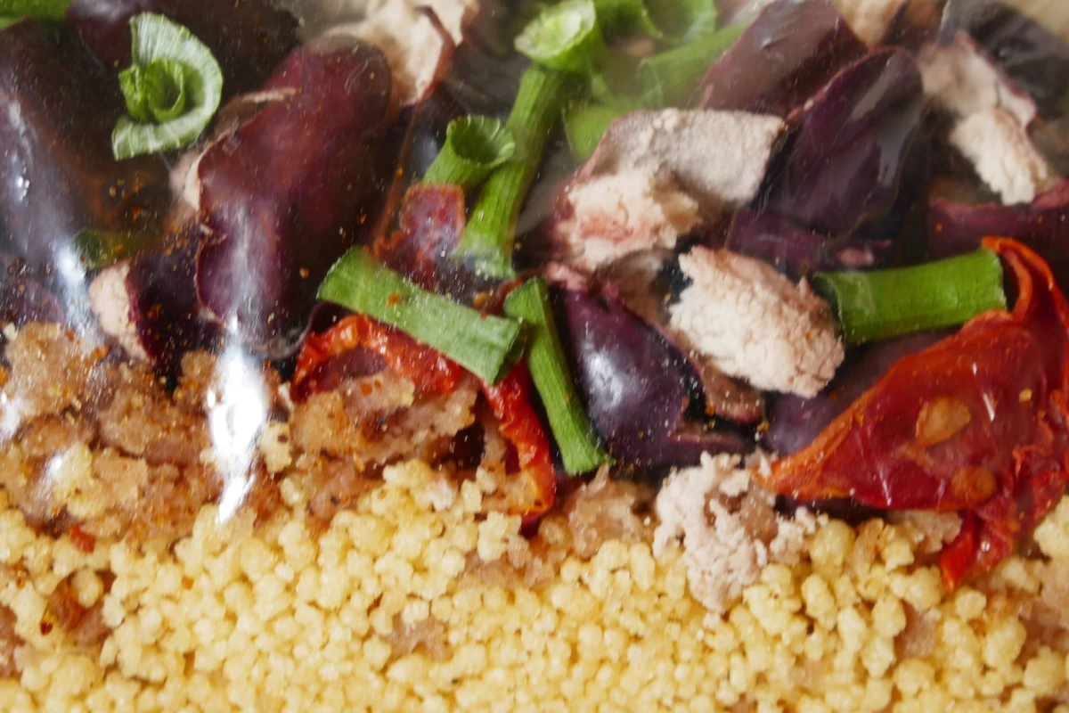 Dehydrated couscous, tomato, chives, kidney beans, and chicken mixed together colourfully.