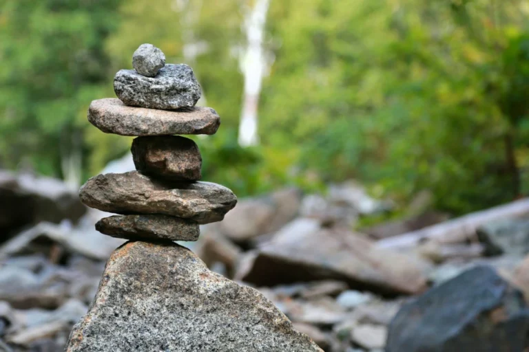 A stack of rocks sits in front of greenery and a waterfall.
