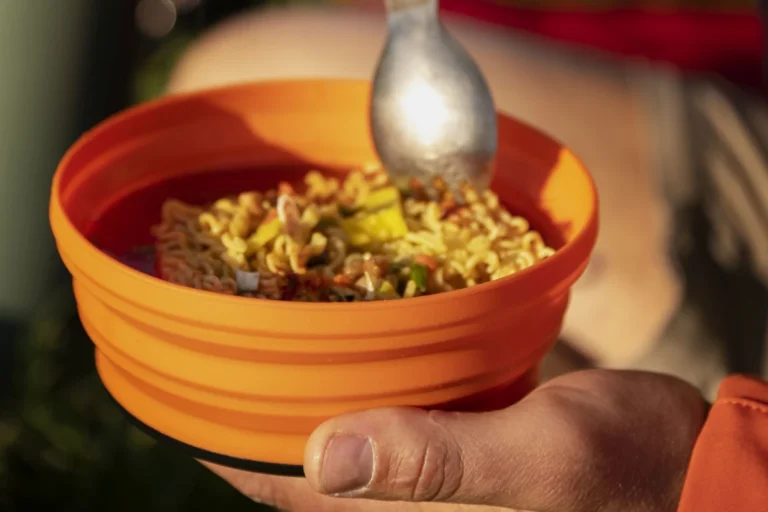 A spoon hovers over and orange bowl filled with noodles.