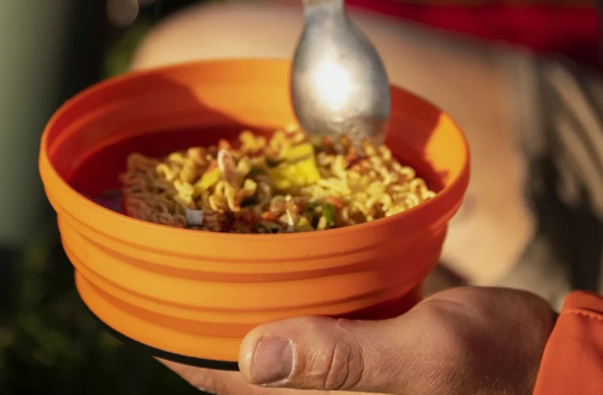 A spoon hovers over and orange bowl filled with noodles.