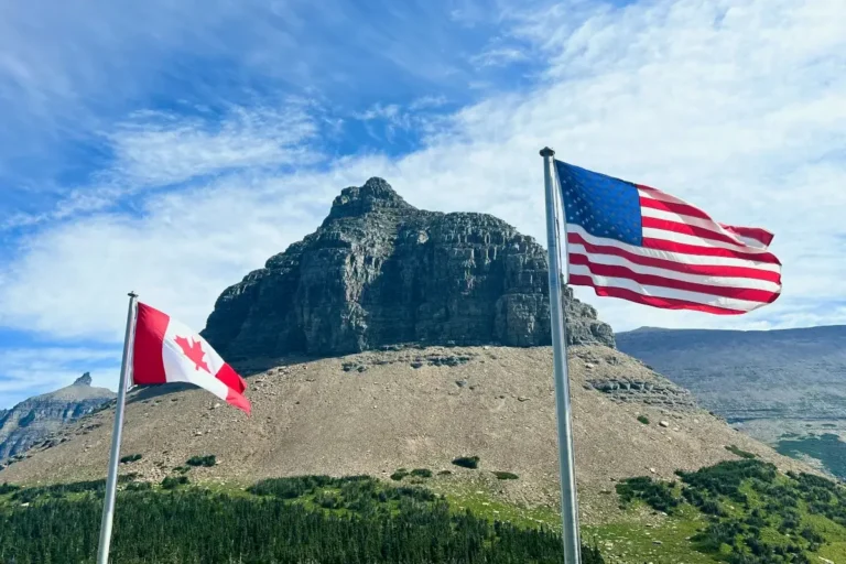 Canadian and America flags blow in the wind before a mountain.