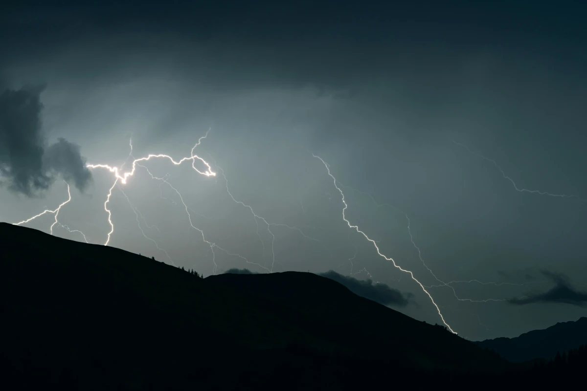 Lightning flashes over silhouetted mountains at night.