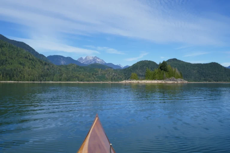 The tip of a kayak on a blue lake points at a rugged mountain.