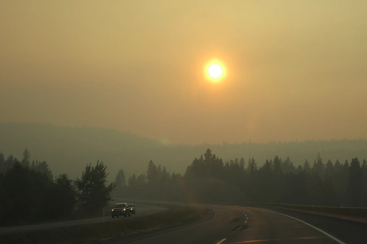 Wildfire smoke gives an orange hue to the sun and a highway landscape