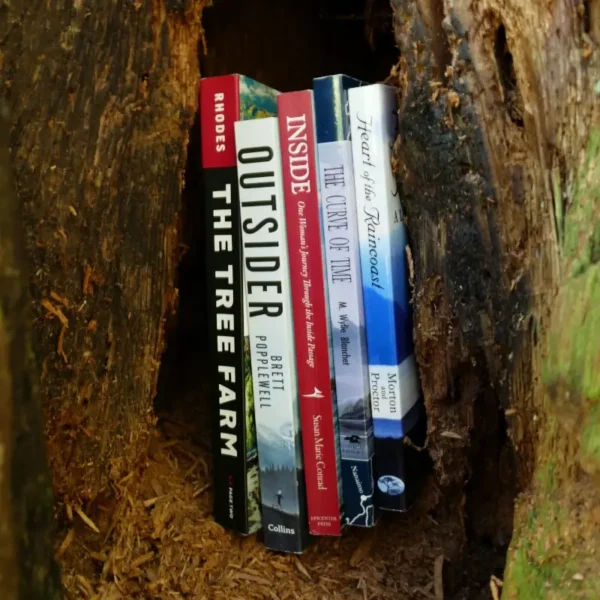 A stack of bc adventure books sits in the hollow of a tree.