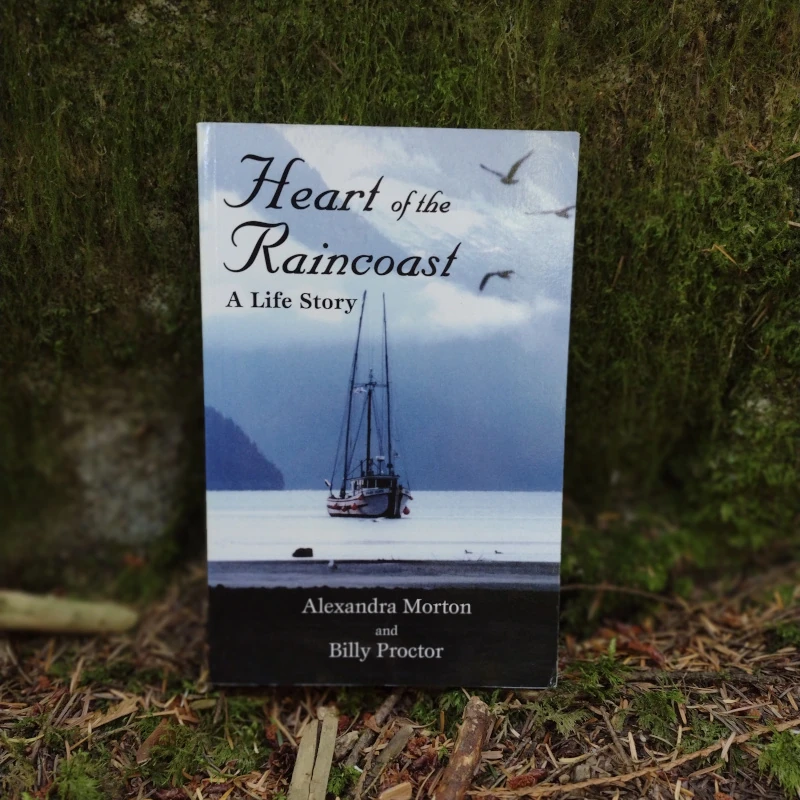 The book "Heart of the Raincoast" leans against a mossy rock.