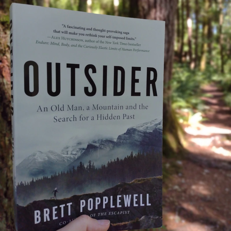 Someone holds up a book in the woods.