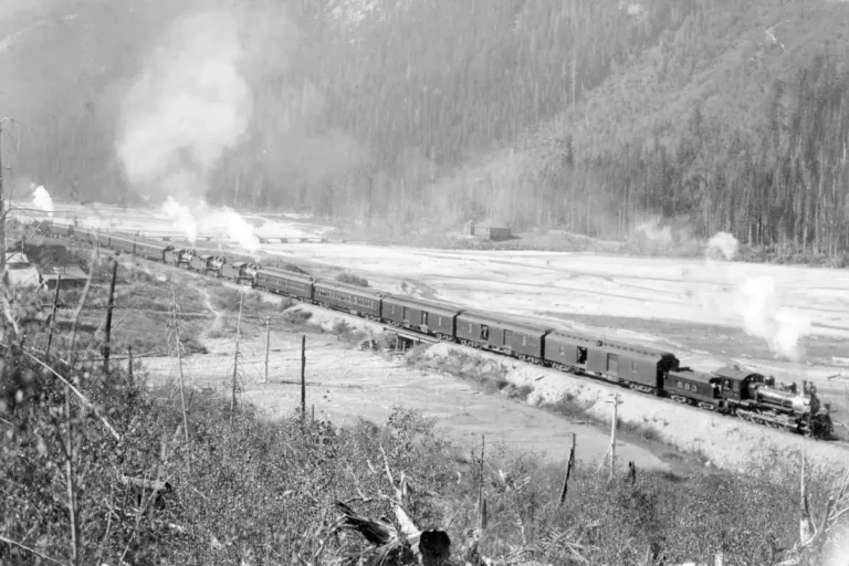 A steam train and cars travels through the BC mountains.