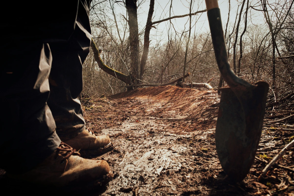 Boots and a shovel are visible in front of a freshly maintained trail.
