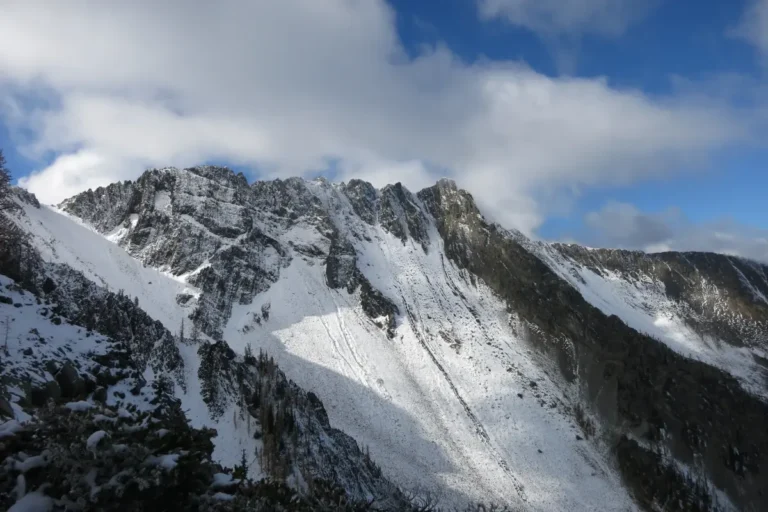 A snowy, jagged peak of the North Cascades against a cloudy blue sky.
