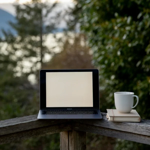 A computer and coffe cup sit on a porch railing.