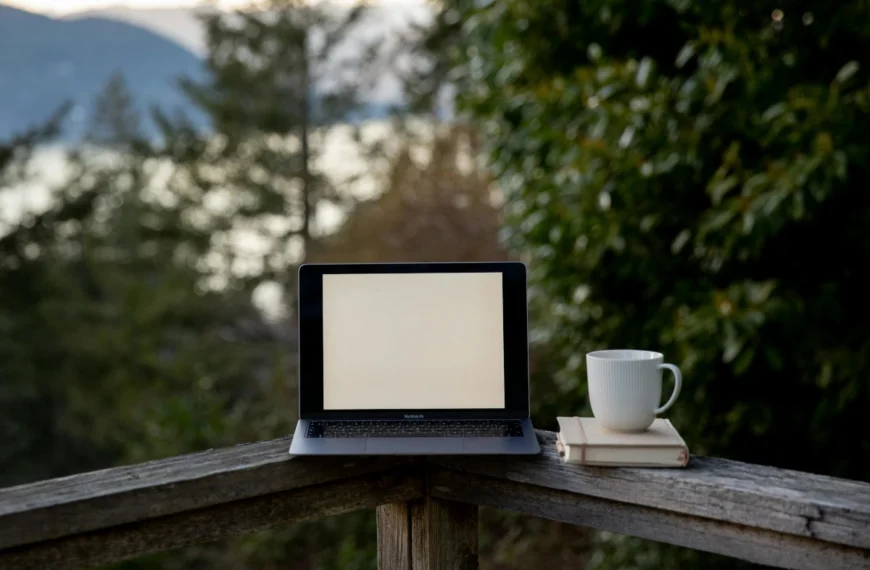 A computer and coffe cup sit on a porch railing.