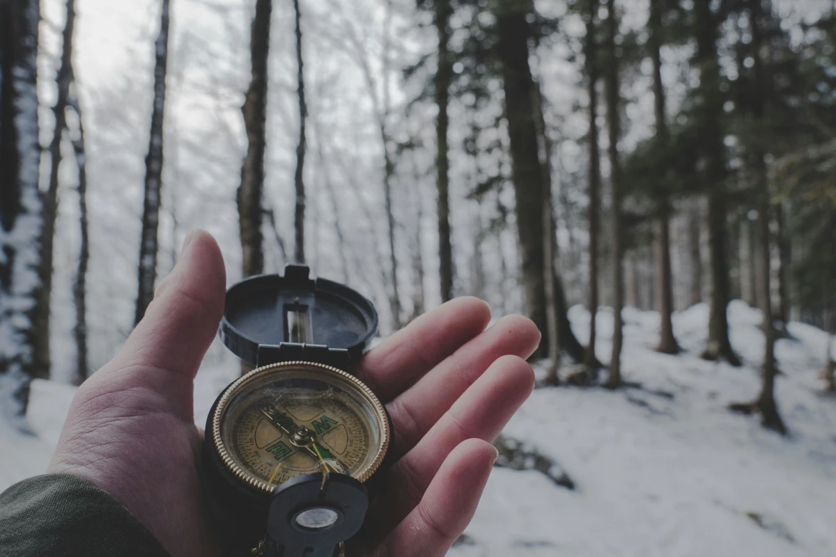 Someone holds a compass up in a snowy forest.