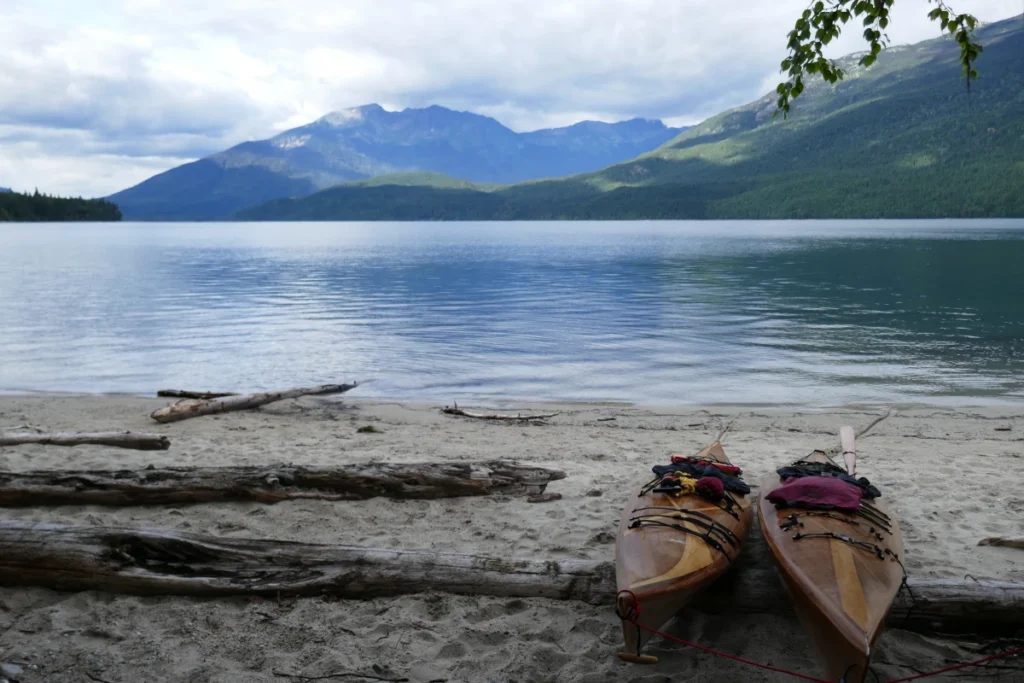 Two kayaks sit on logs on the shore of a lake.