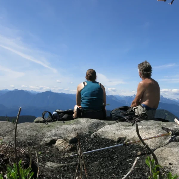 Two people sit on a mountain viewpoint.