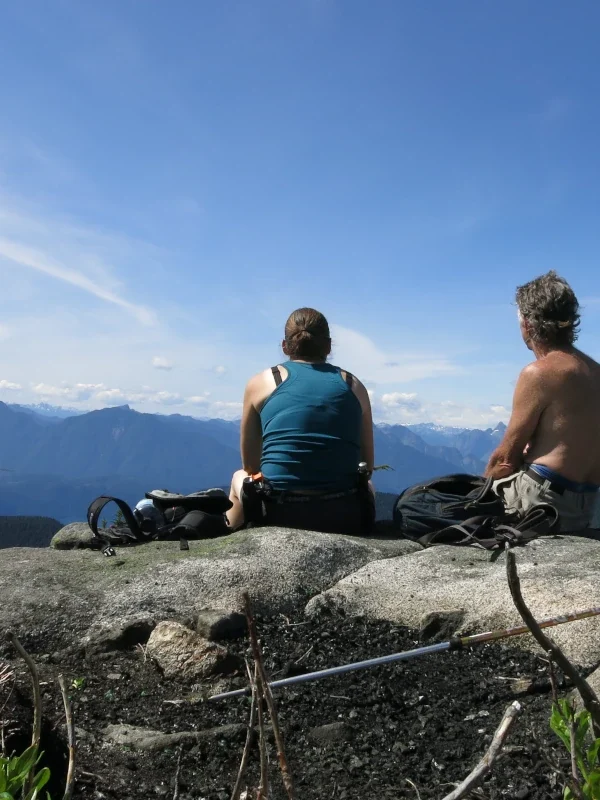 Two people sit on a mountain viewpoint.