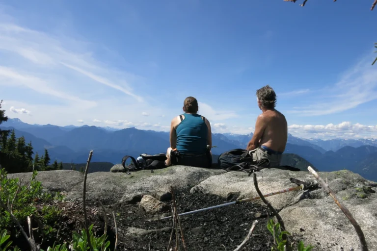 Two people sit on a mountain viewpoint.