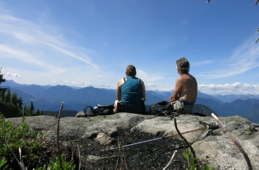 Two people sit on a mountain viewpoint.