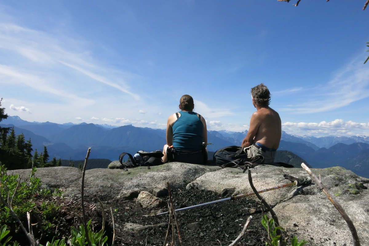Two people sit on a mountain viewpoint.