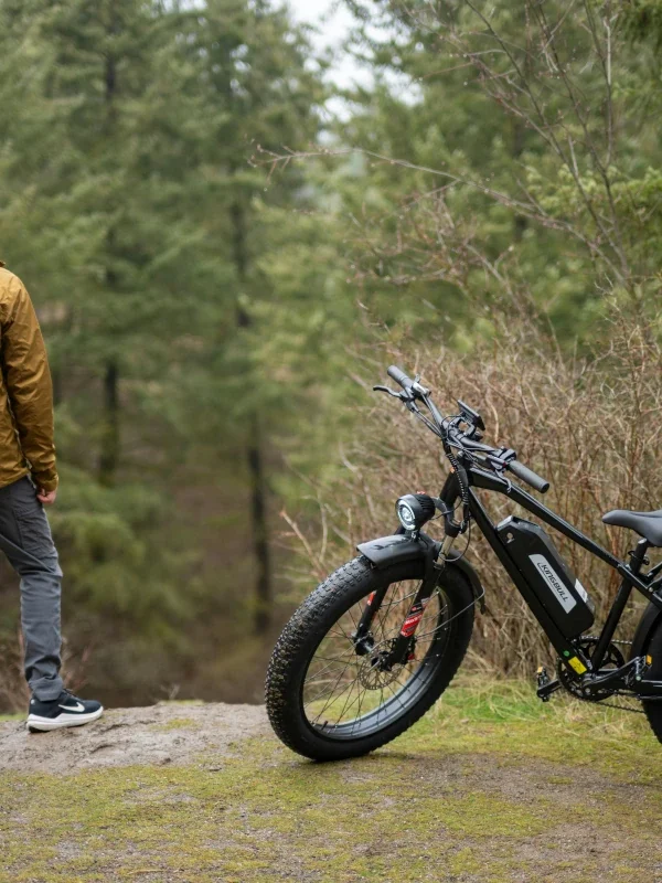 A man stands next to an e-bike in the forest.