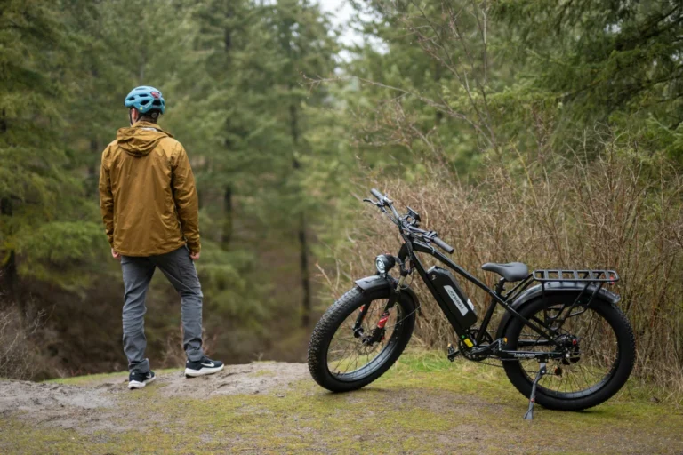 A man stands next to an e-bike in the forest.