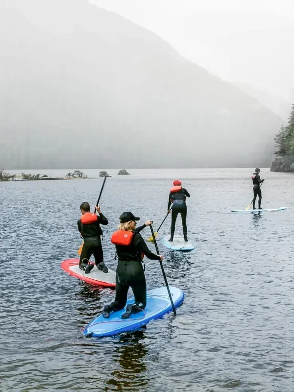 Paddleboarders wearing PFDs paddle on a cloudy lake.