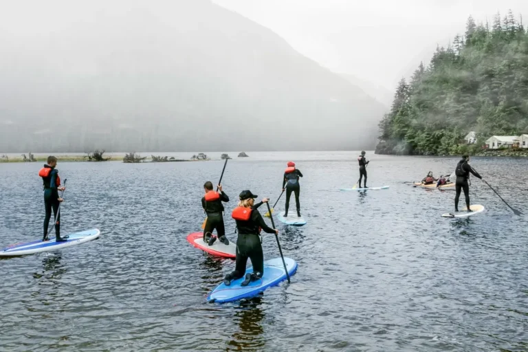 Paddleboarders wearing PFDs paddle on a cloudy lake.
