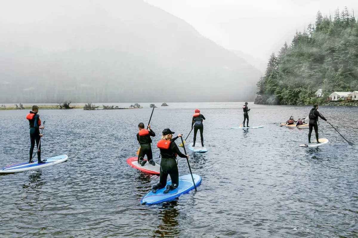 Paddleboarders wearing PFDs paddle on a cloudy lake.