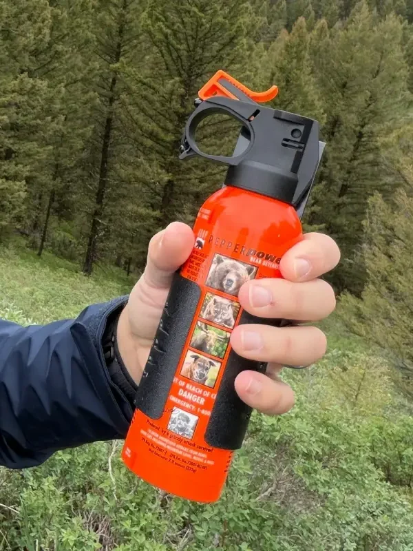 A bear spray canister is held against a forest backdrop.